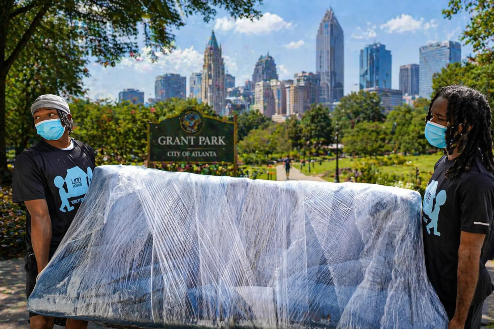 LIOO Moving movers carrying a wrapped couch in Grant Park Atlanta with the skyline in the background