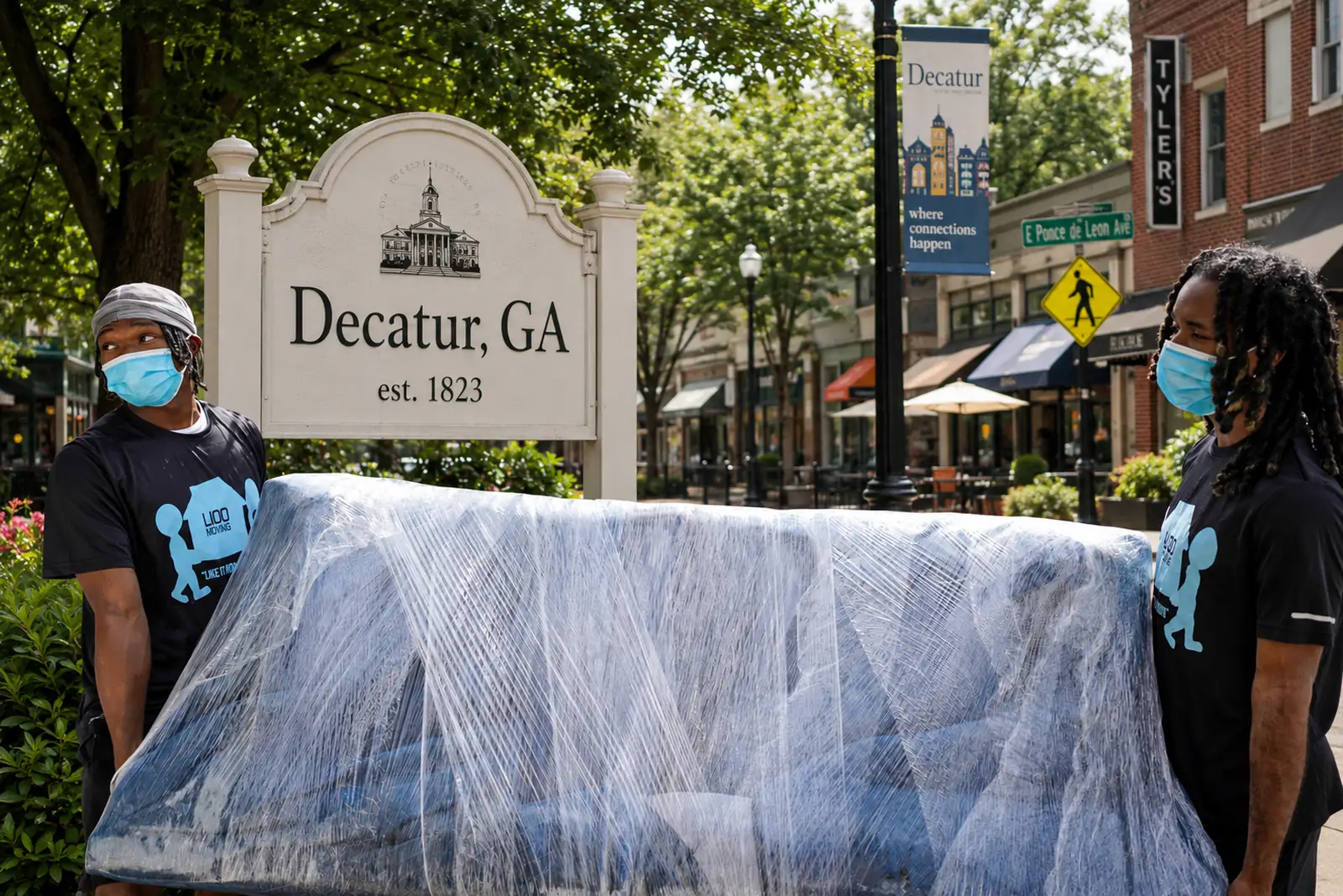 Movers carry a shrink-wrapped couch beside the Decatur, Georgia welcome sign downtown