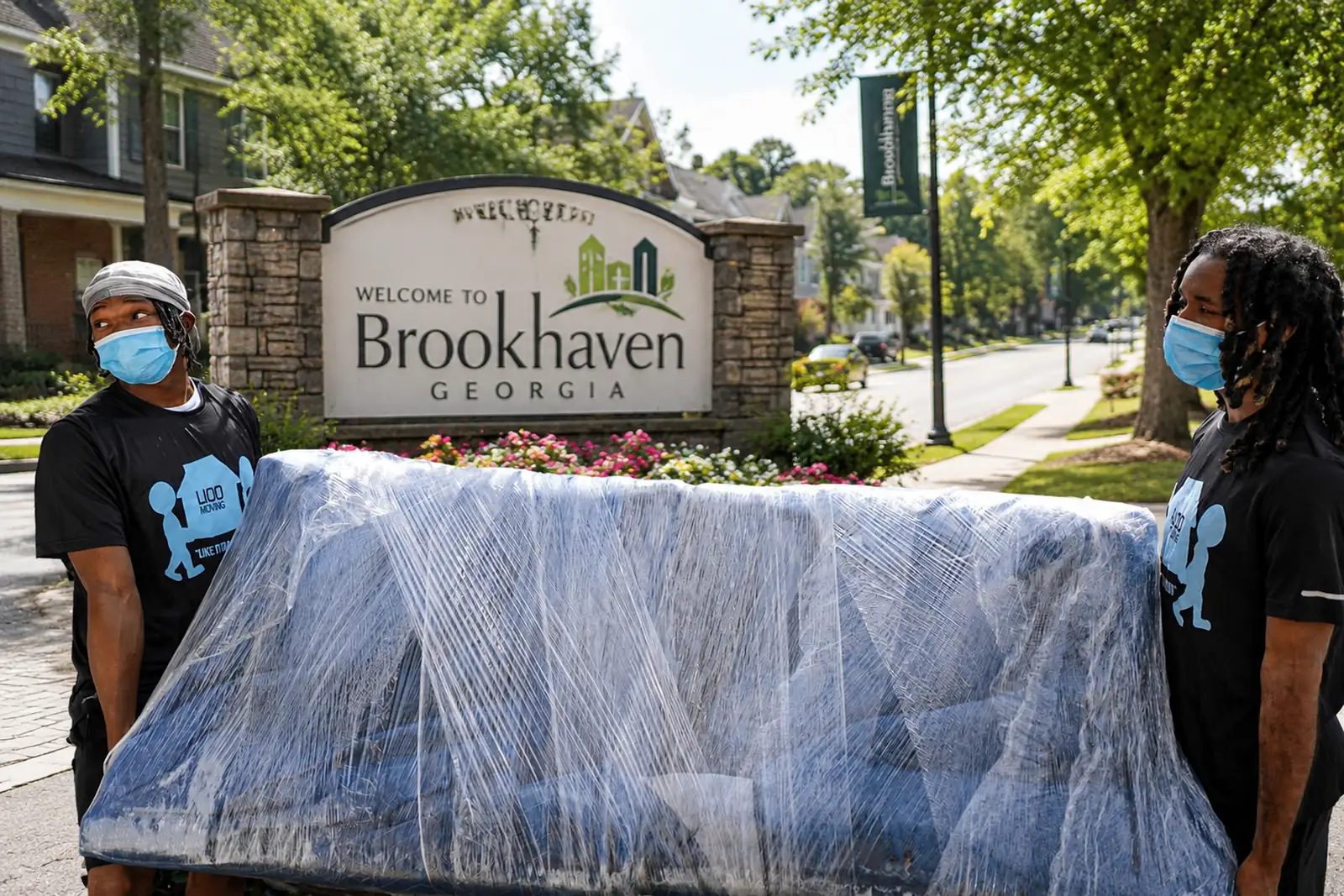 Two movers carry a wrapped sofa past the Brookhaven welcome sign in Georgia