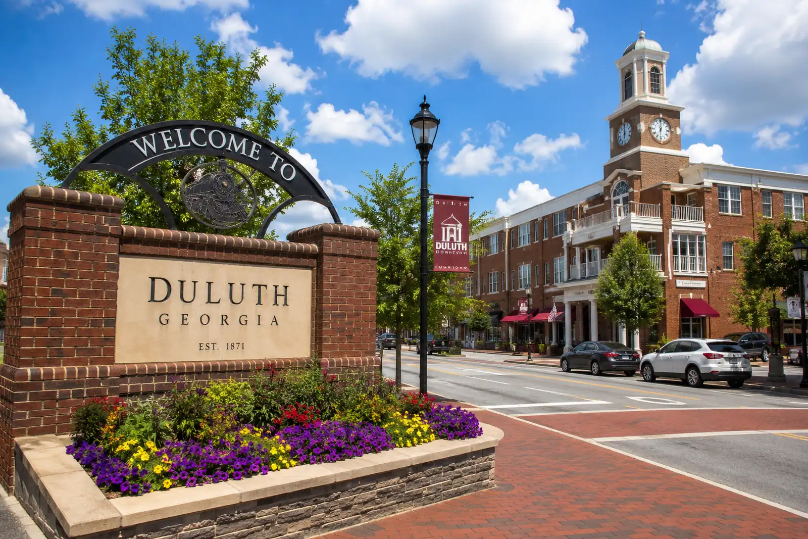 Historic downtown streetscape with brick buildings, landscaped entrance sign, and tree-lined street in Duluth.