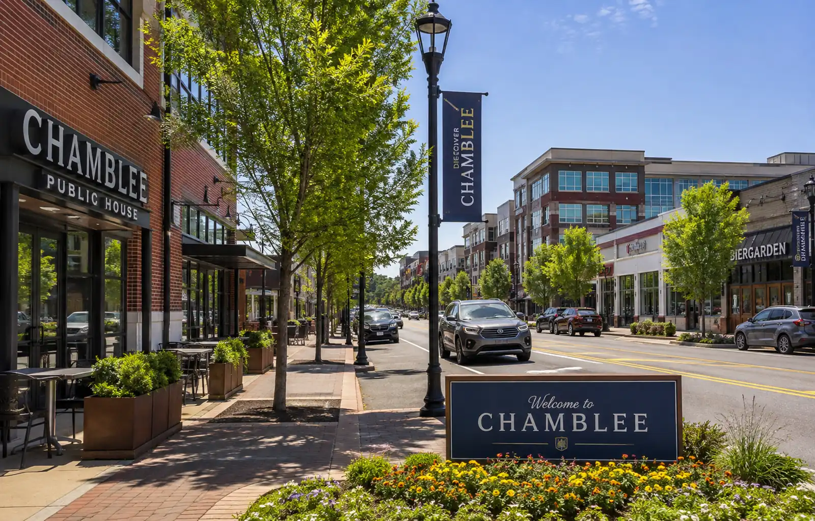 Tree-lined Chamblee commercial street with storefronts, sidewalks, vehicles, and a Welcome to Chamblee sign.