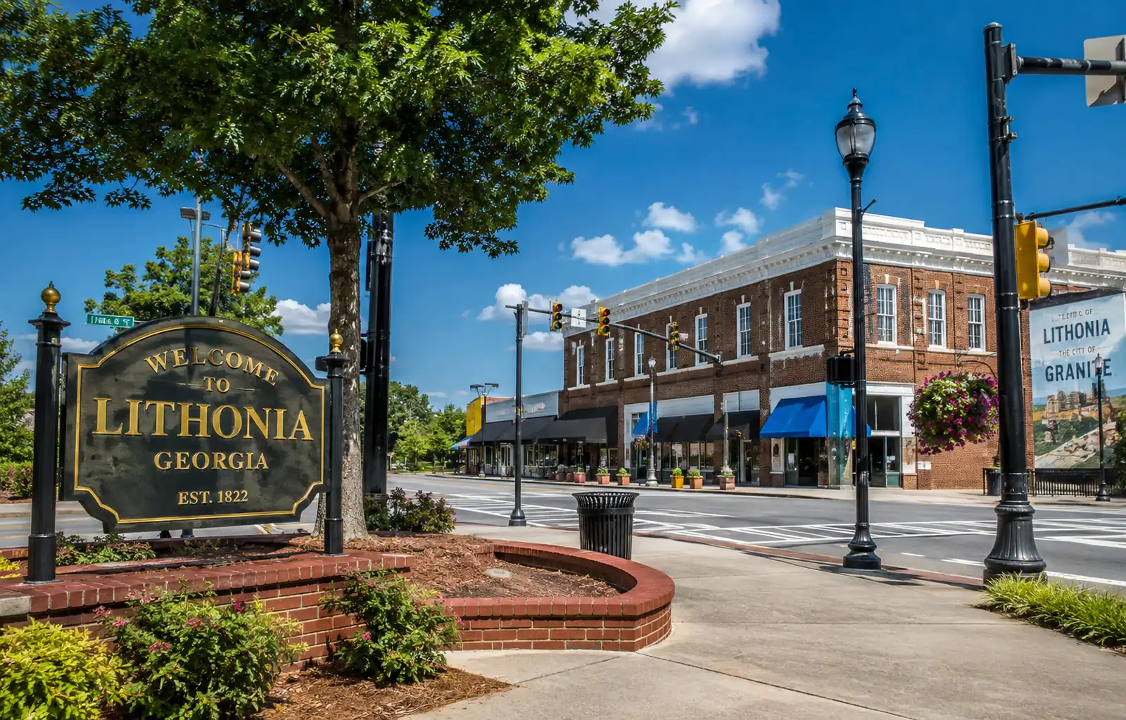 Brick storefronts, marked crosswalks, and streetlights frame a downtown Lithonia commercial intersection.