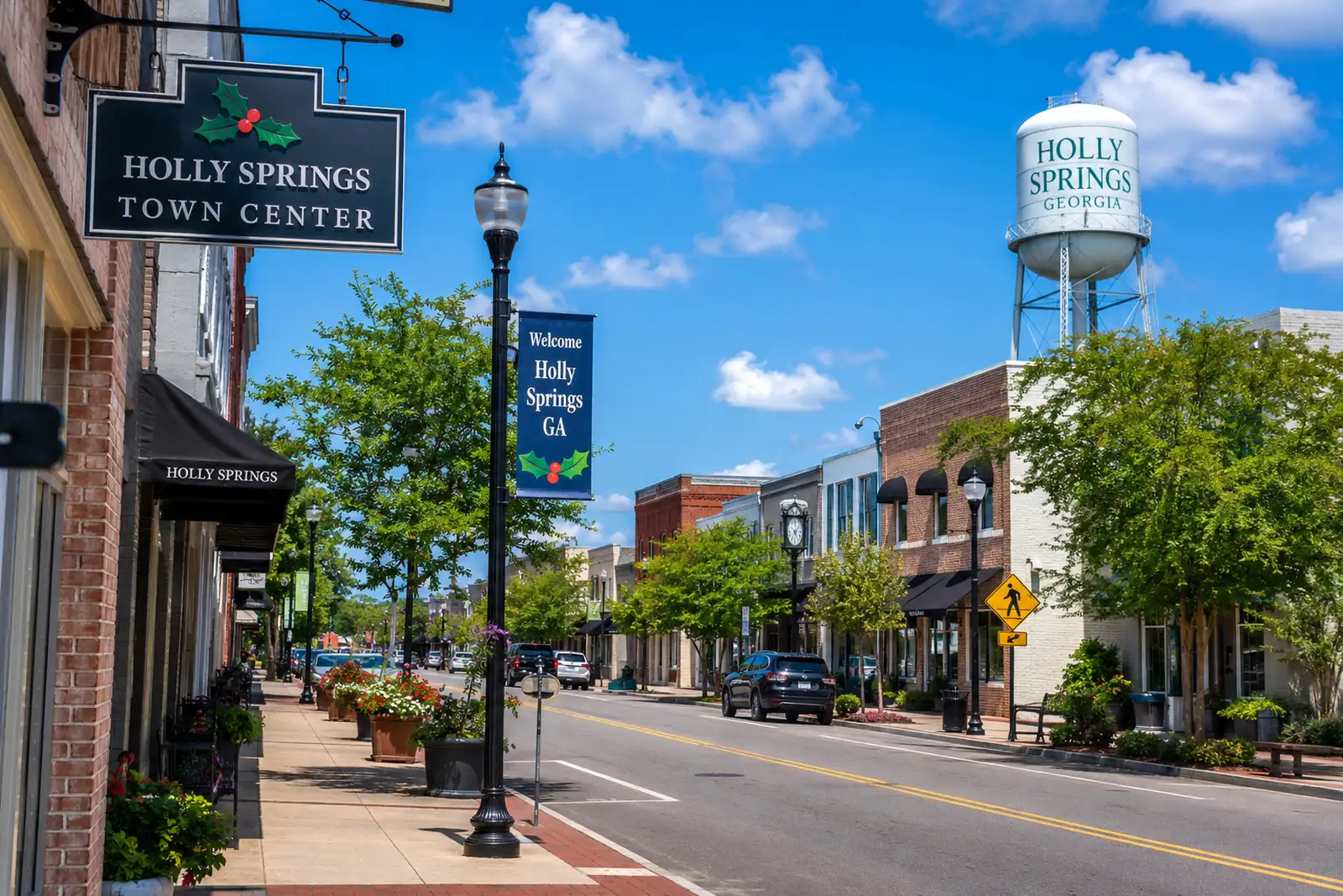 Brick storefronts and streetlamps line a downtown Holly Springs, Georgia commercial street beneath a blue sky.