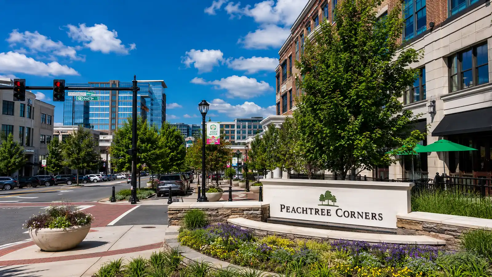 Peachtree Corners streetscape with landscaped sidewalks, commercial buildings, roadway traffic, and a monument sign