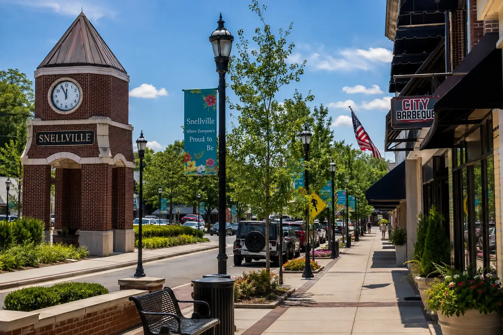 Brick clock tower overlooking a landscaped downtown street with storefronts, sidewalks, trees, and decorative banners in Snellville.